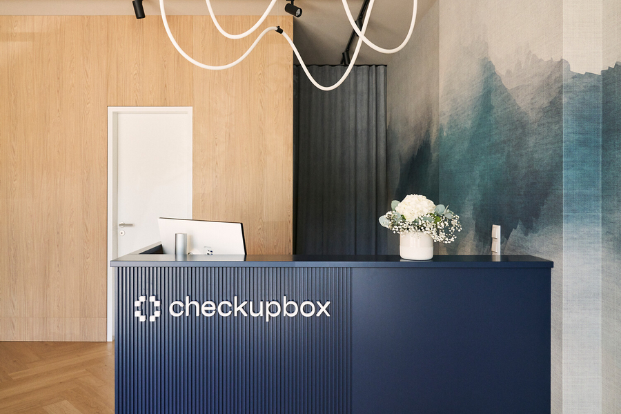 Empfangstresen der checkupbox mit blauen Wänden, ausgestattet mit einem Computer und Stühlen.